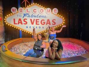 Three happy Black women in a pit of poker tokens with a Vegas sign in the background