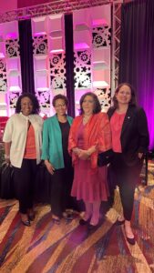 Four women standing and smiling at an event honoring Enid Draluck and other women of excellence. 