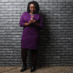 Black woman in a purple dress looking at party favors and smiling